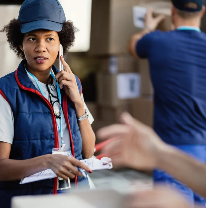 black-female-deliverer-communicating-with-coworker-while-talking-mobile-phone-organizing-package-delivery